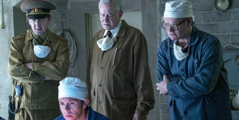 The cast of 'Chernobyl' examining something with masks around their necks.