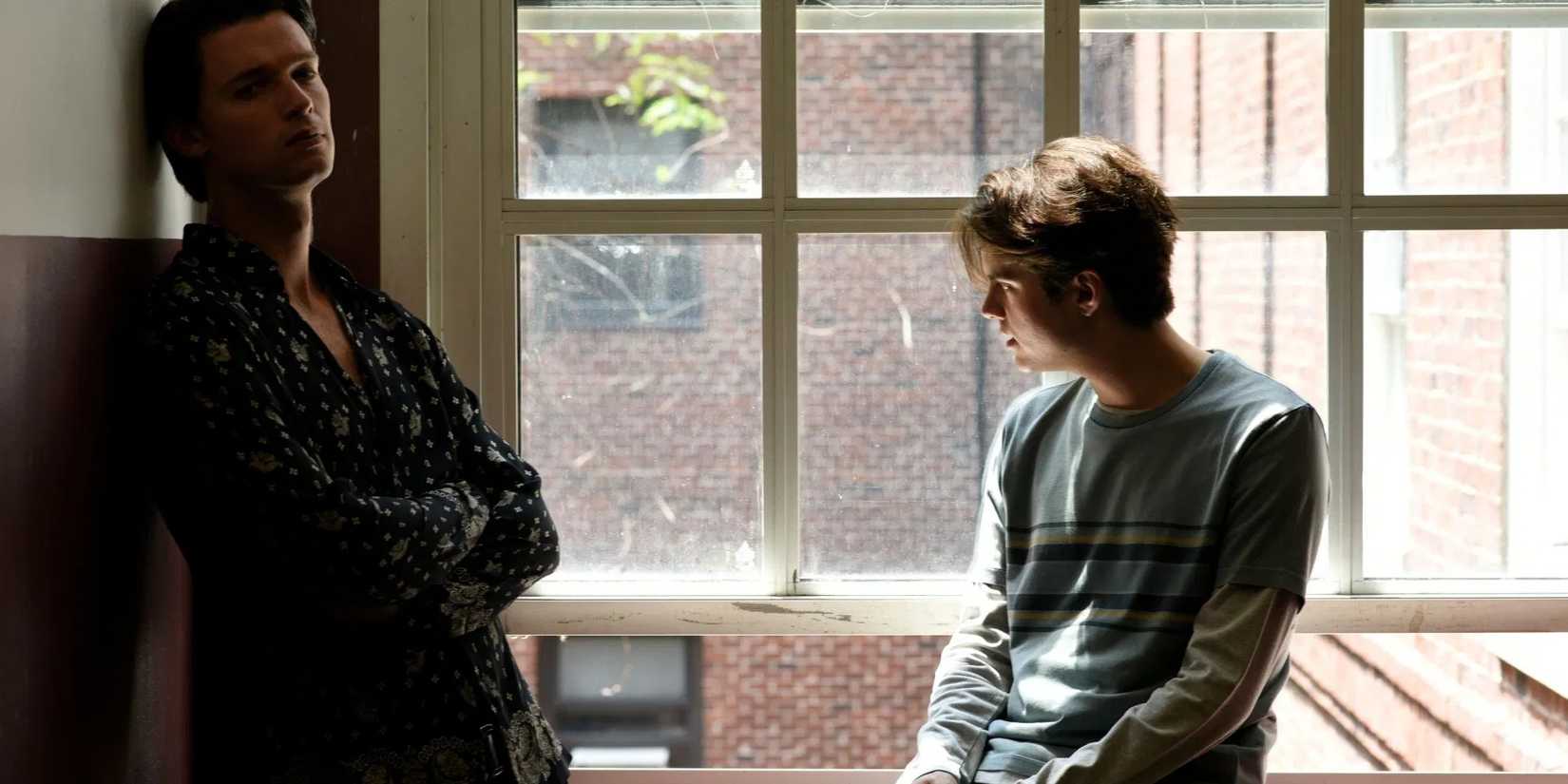 Daniel and Luke, played by actors Patrick Schwarzenegger and Miles Robbins, stand moodily by a window in Daniel Isn't Real.