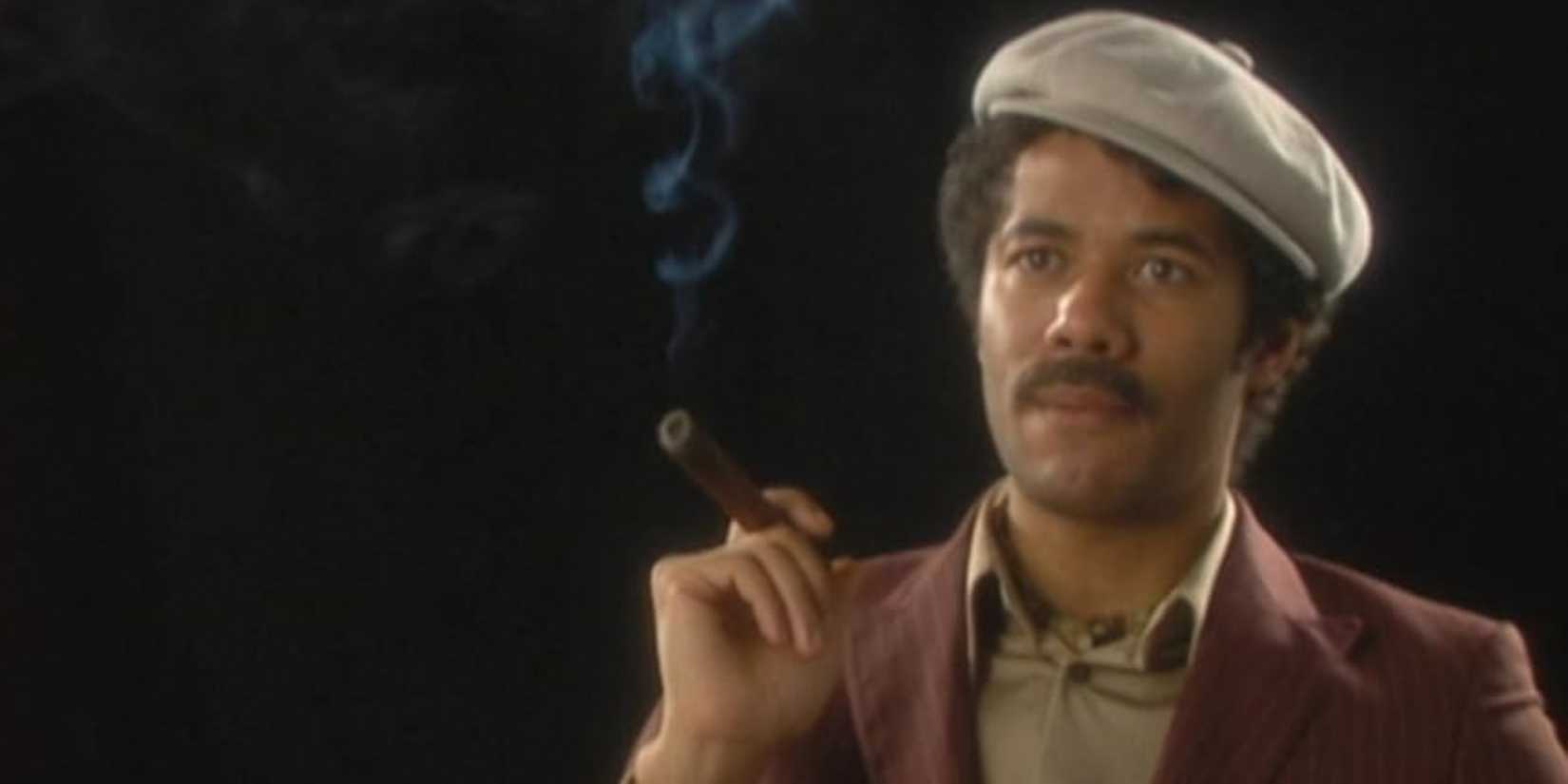 Richard Ayoade as Dean Learner in a beret smoking a cigar in an interview in Garth Marenghi's Darkplace.