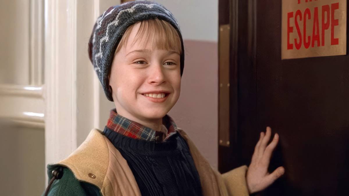 Macaulay Culkin as Kevin McCallister smiling next to an Escape door in Home Alone 2 Lost in New York