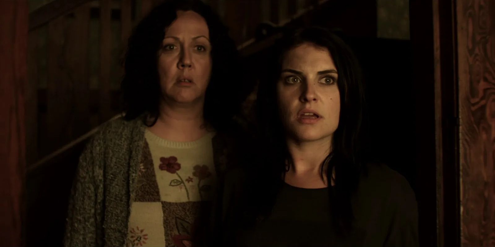 Kylie and Miriam, played by actors Morgana O'Reilly and Rima Te Wiata, stand in a shadowy doorway looking worriedly at something in Housebound.