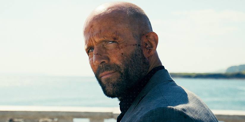 Jason Statham as Adam Clay with a bloodied face looks up with a slight smile in The Beekeeper