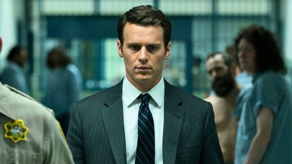 Jonathan Groff in a suit and tie walking through a prison in Mindhunter.