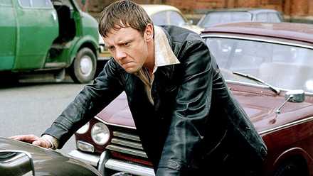 Sam Tyler leaning against a car hood with an angry expression in Life on Mars.