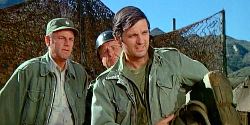 Alan Alda as Hawkeye looking at an object with others behind him in M*A*S*H Season 1.