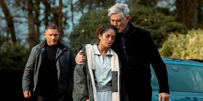 Conrad Harrigan (Pierce Brosnan) holding Seraphina (Mandeep Dhillon) close with Harry (Tom Hardy) behind them in MobLand