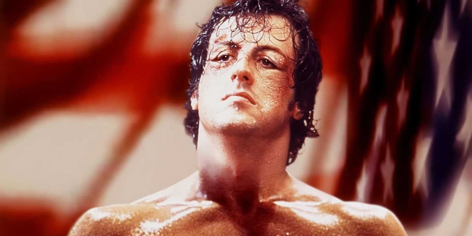 Actor Sylvester Stallone as Rocky Balboa in Rocky, looking exhausted but defiant in front of an American flag.