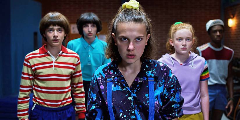 The cast of Stranger Things look just past the camera with worried expressions. 