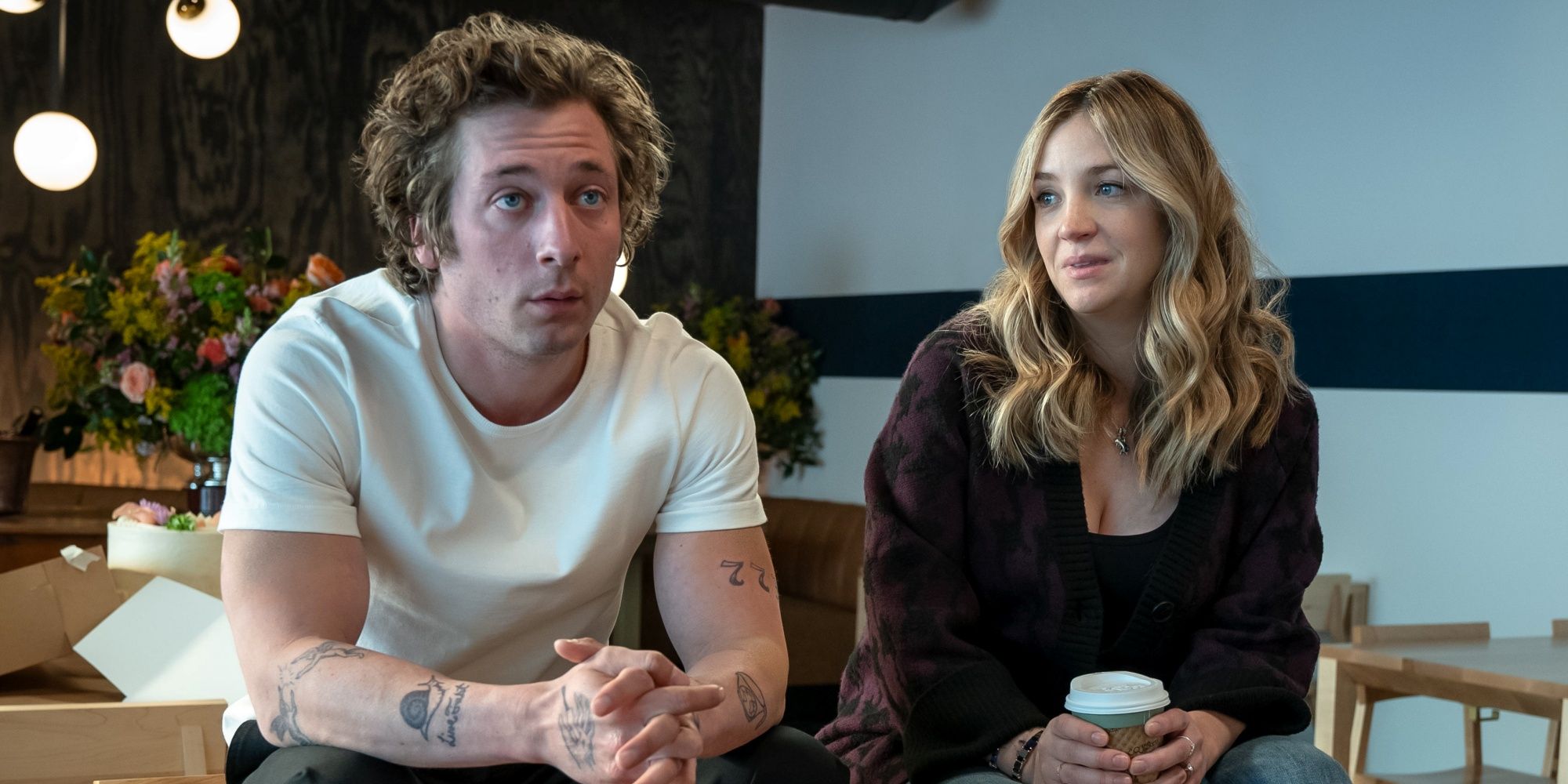 Abby Elliott as Sugar sitting in the empty restaurant next to Jeremy Allen White as Carmy in The Bear Season 2.