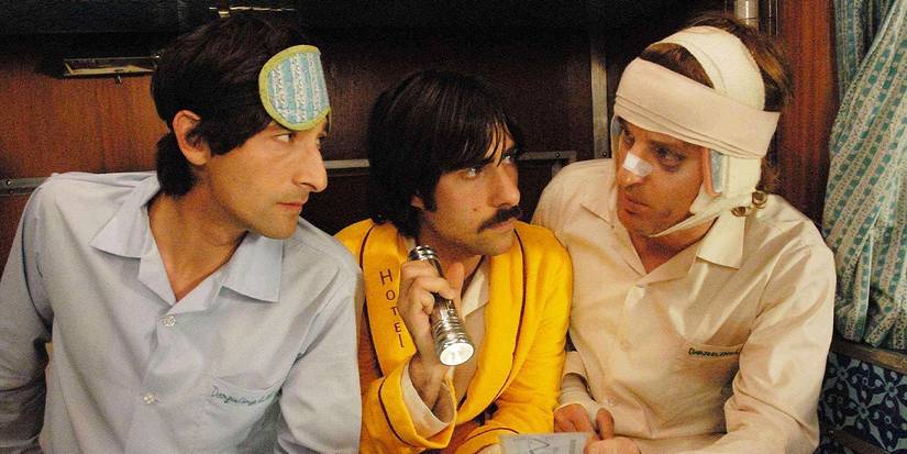 The Whitman brothers played by Owen Wilson, Adrien Brody, and Jason Schwartzman in pajamas looking at a piece of paper with a flashlight in The Darjeeling Limited.