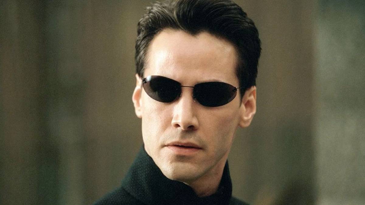 A close-up of Keanu Reeves as Neo looking to the distance with sunglasses on in The Matrix.