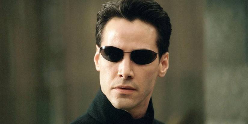 A close-up of Keanu Reeves as Neo looking to the distance with sunglasses on in The Matrix.