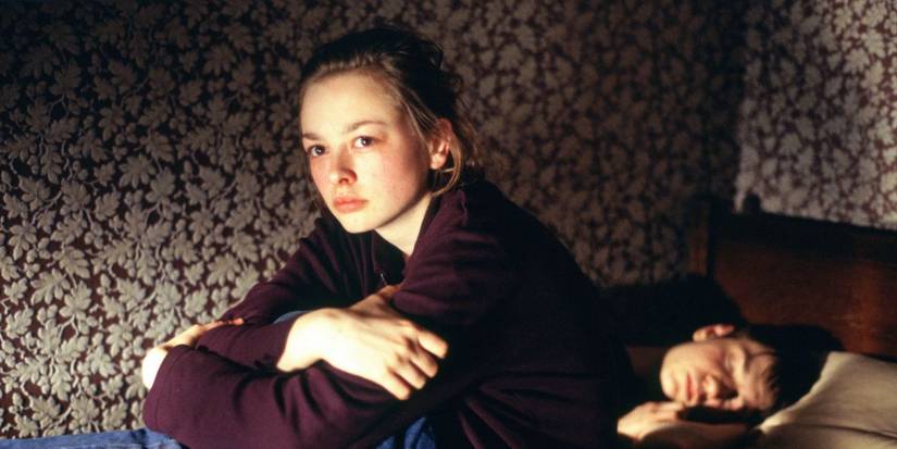 A young girl sitting on a bed with a sleeping guy beside her in the war zone