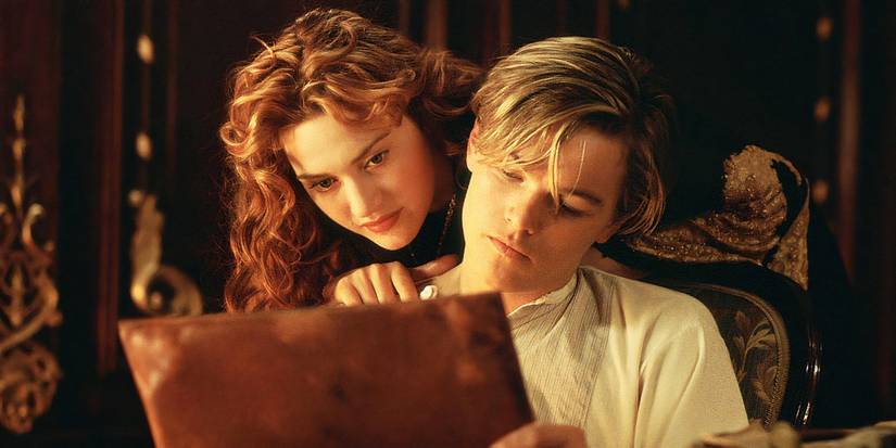 Kate Winslet as Rose looks over Leonardo DiCaprio's shoulder at a drawing in Titanic.