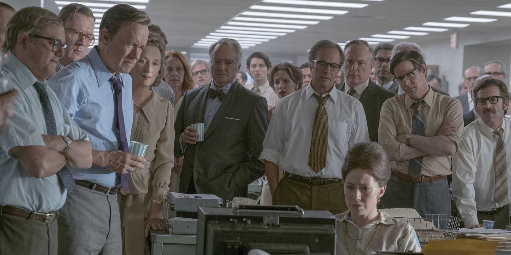 Tom Hanks stands, surrounded by the staff of The Washington Post, as Carrie Coon reads the latest report on their Supreme Court case in Steven Spielberg's 'The Post'