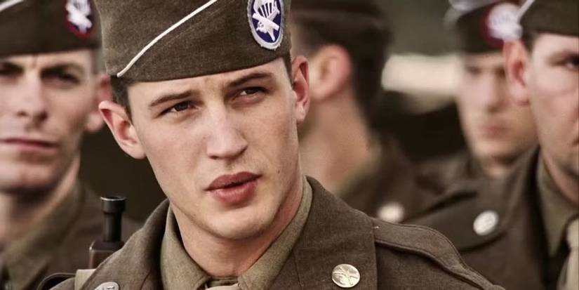 Tom Hardy sebagai seorang tentara melihat seseorang di luar kamera, berdiri bersama tentara lain di Band of Brothers.