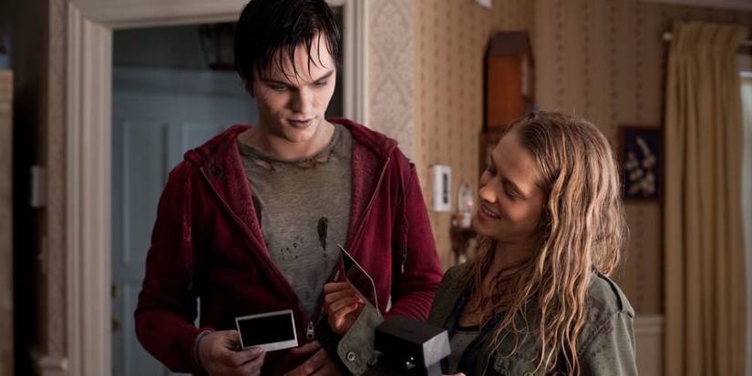 Nicholas Hoult and Teresa Palmer stand together in a house, looking at polaroids in 'Warm Bodies'.