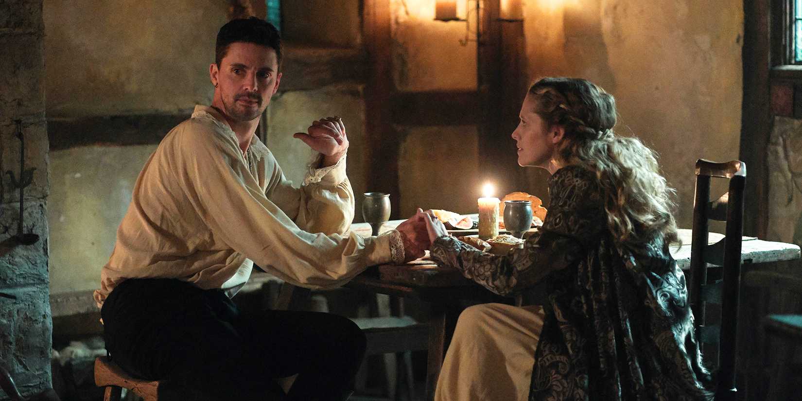 A man and woman sit by candlelight holding hands in A Discovery of Witches.