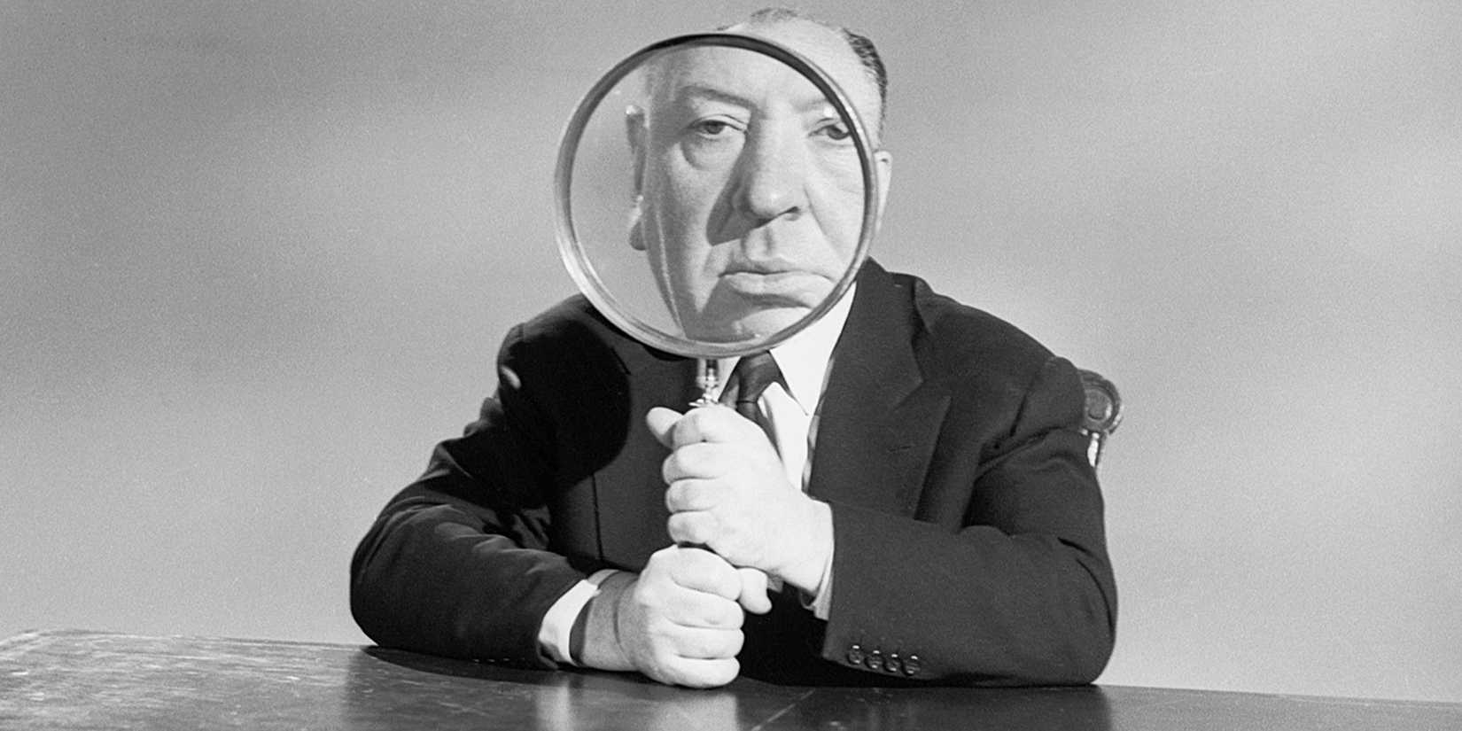 Alfred Hitchcock looking through a huge magnifying glass 