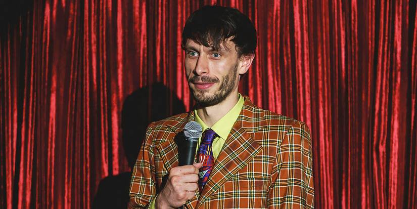 Donny on stage holding a microphone in front of a red curtain in Netflix's Baby Reindeer.
