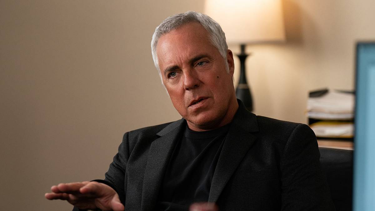 Harry Bosch sitting in a chair talking with his hand out in Bosch.