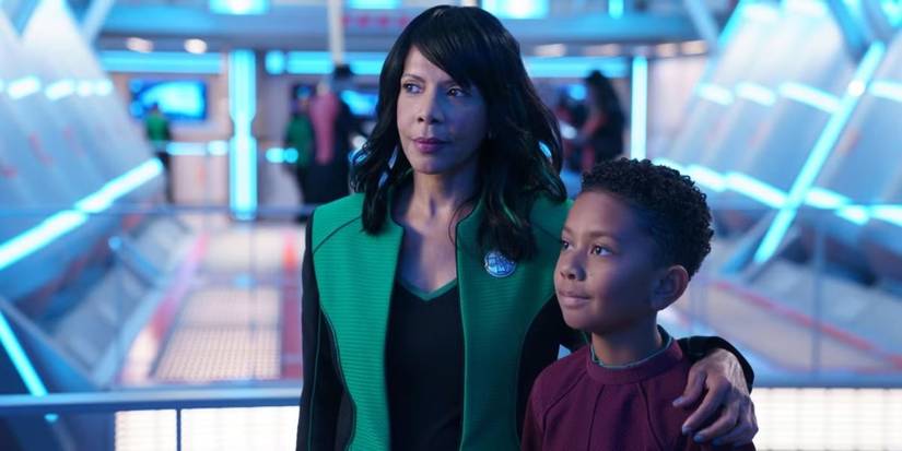 Penny Johnson Jerald as Dr. Claire Finn stands casually with her arm around her son in The Orville. 
