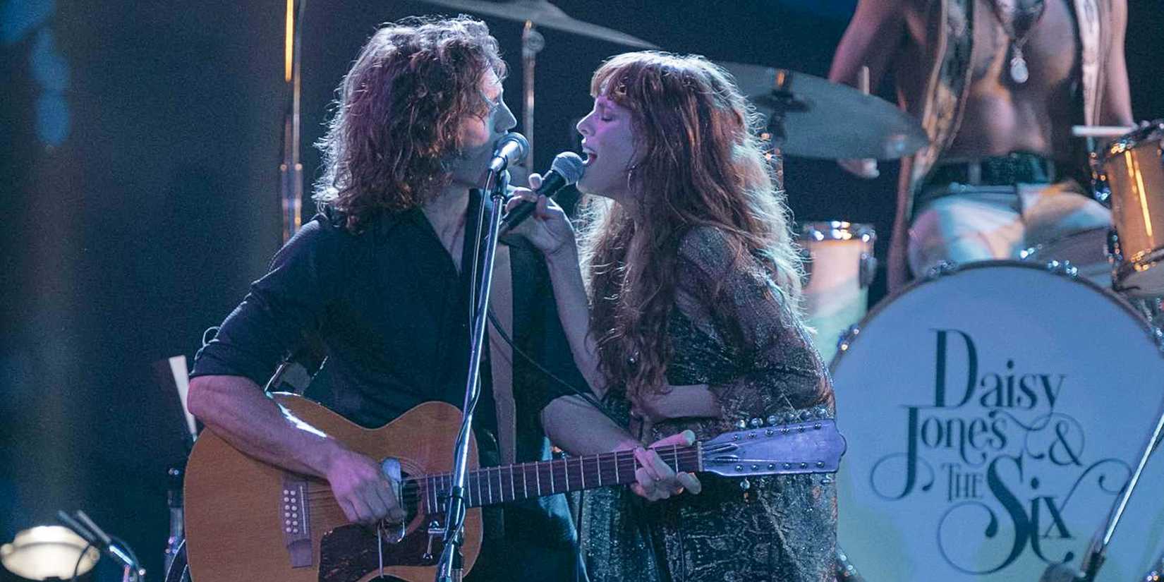 Billy Dunne and Daisy Jones singing and playing guitar onstage together in Daisy Jones and the Six.