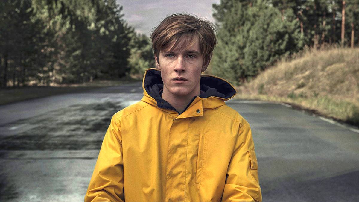 Jonas standing in the middle of a rural road with a raincoat on in the series Dark.