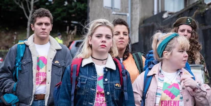 Vários personagens de Derry Girls em pé com jaquetas e mochilas.
