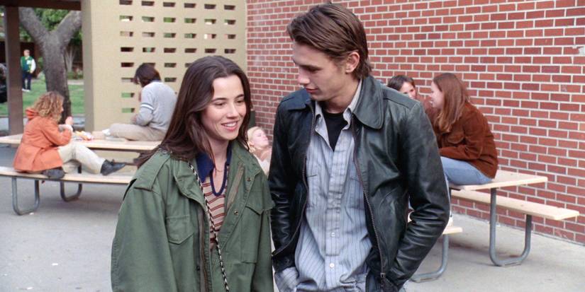 Lindsay Weir (Linda Cardellini) and Daniel Desario (James Franco) stand closely by each other in the schoolyard of their high school in 'Freaks and Geeks' (1999-2000).