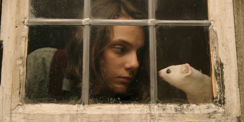 Dafne Keen as Lyra looking at a mouse behind a window in His Dark Materials.