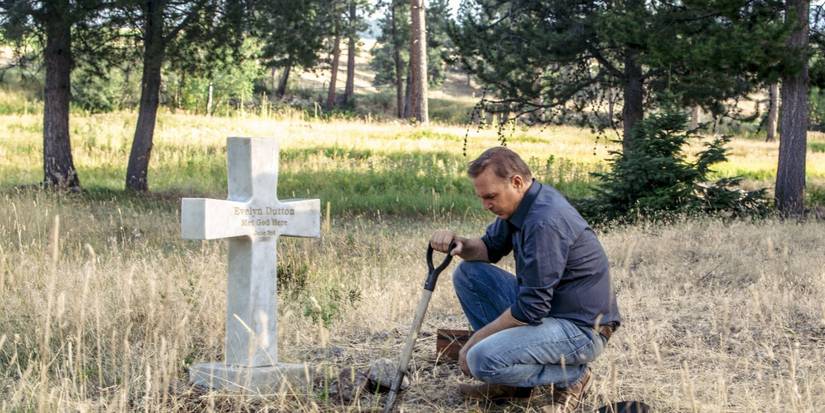 Kevin Costner as John Dutton, kneeling next to a grave and holding a shovel in Yellowstone.