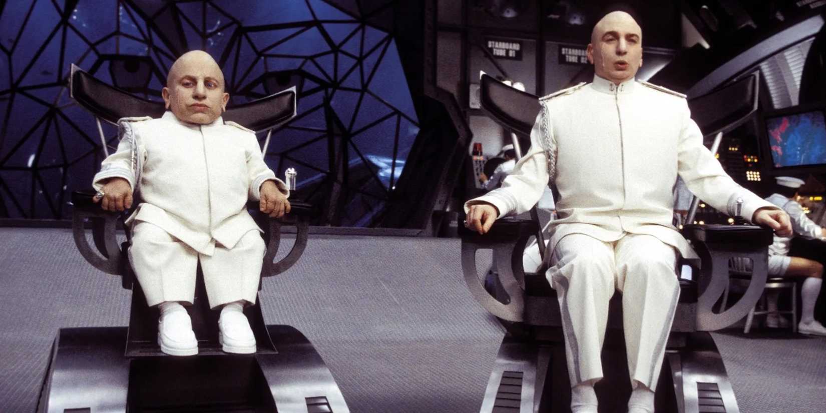 Mini Me and Dr. Evil, played by actors Verne Troyer and Mike Myers, sit in electronic chairs in matching white outfits in Austin Powers in Goldmember.
