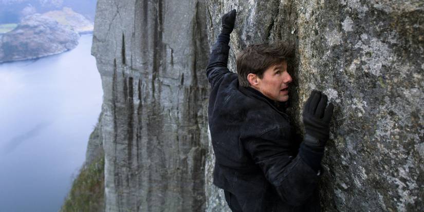 Tom Cruise as Ethan Hunt hanging onto a cliff near the end of Mission_ Impossible – Fallout (2018)