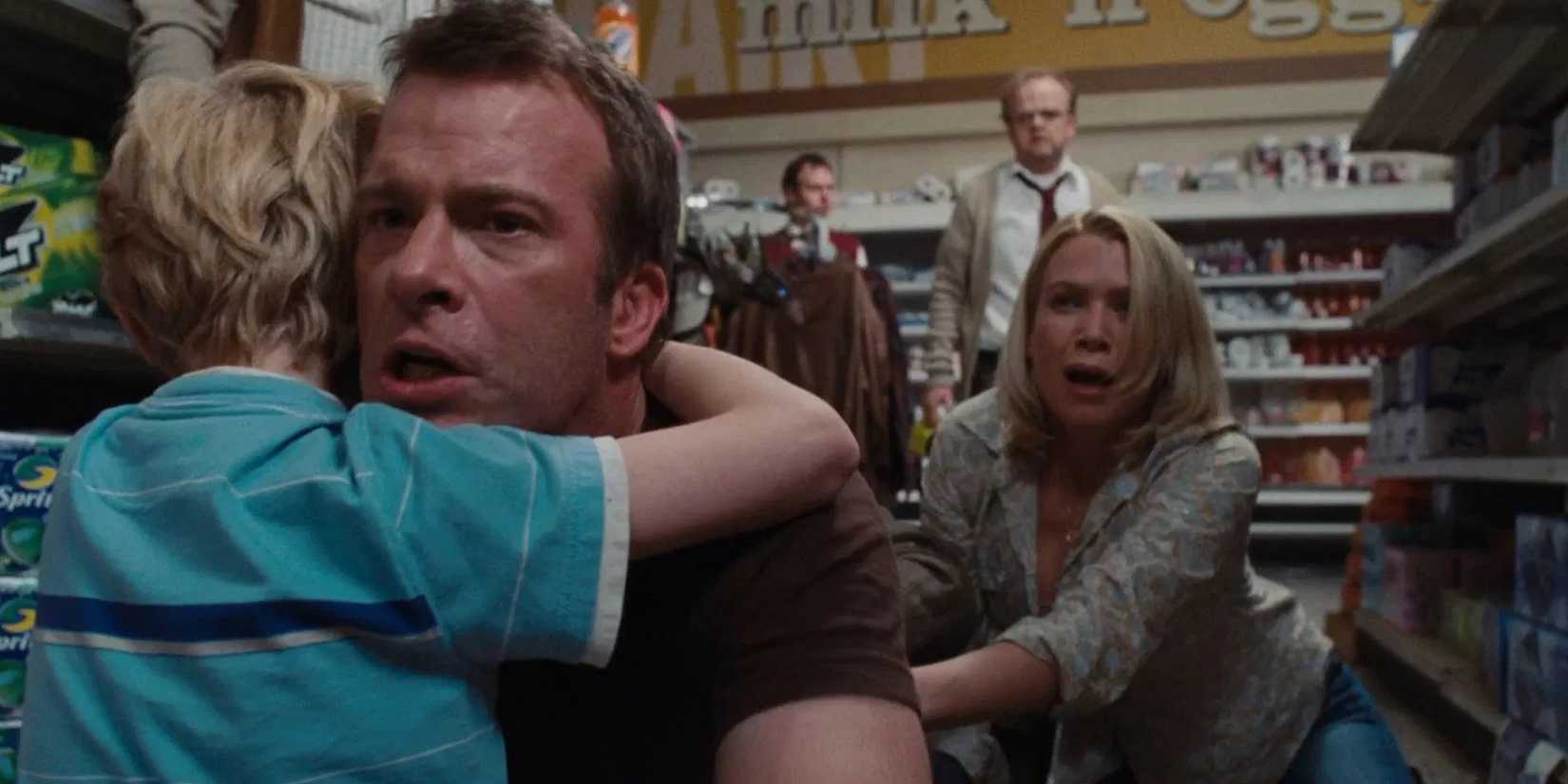 Thomas Jane, on the floor of a supermarket, worriedly holding his young son, with a few people behind them in The Mist.