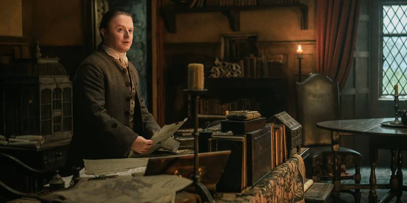 Conor MacNeill as Ned Gowan looking to the side standing at a desk in an office in Outlander: Blood of My Blood