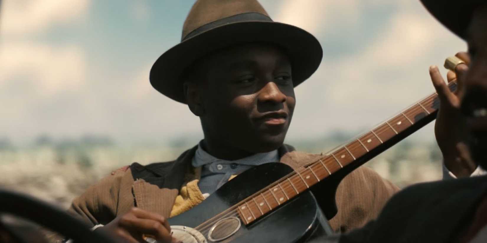 Sammie playing guitar in the backseat of a driving car in Sinners