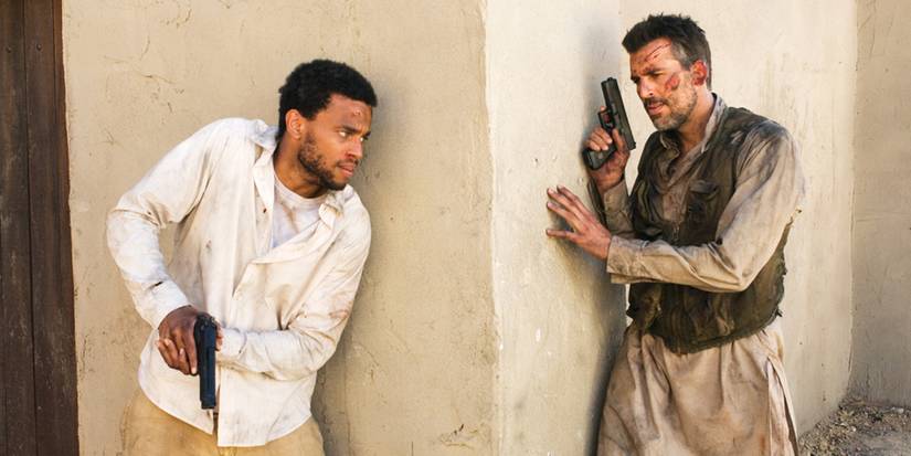 Darwyn and Faris each hold guns on opposing sides of a corner in Sleeper Cell.