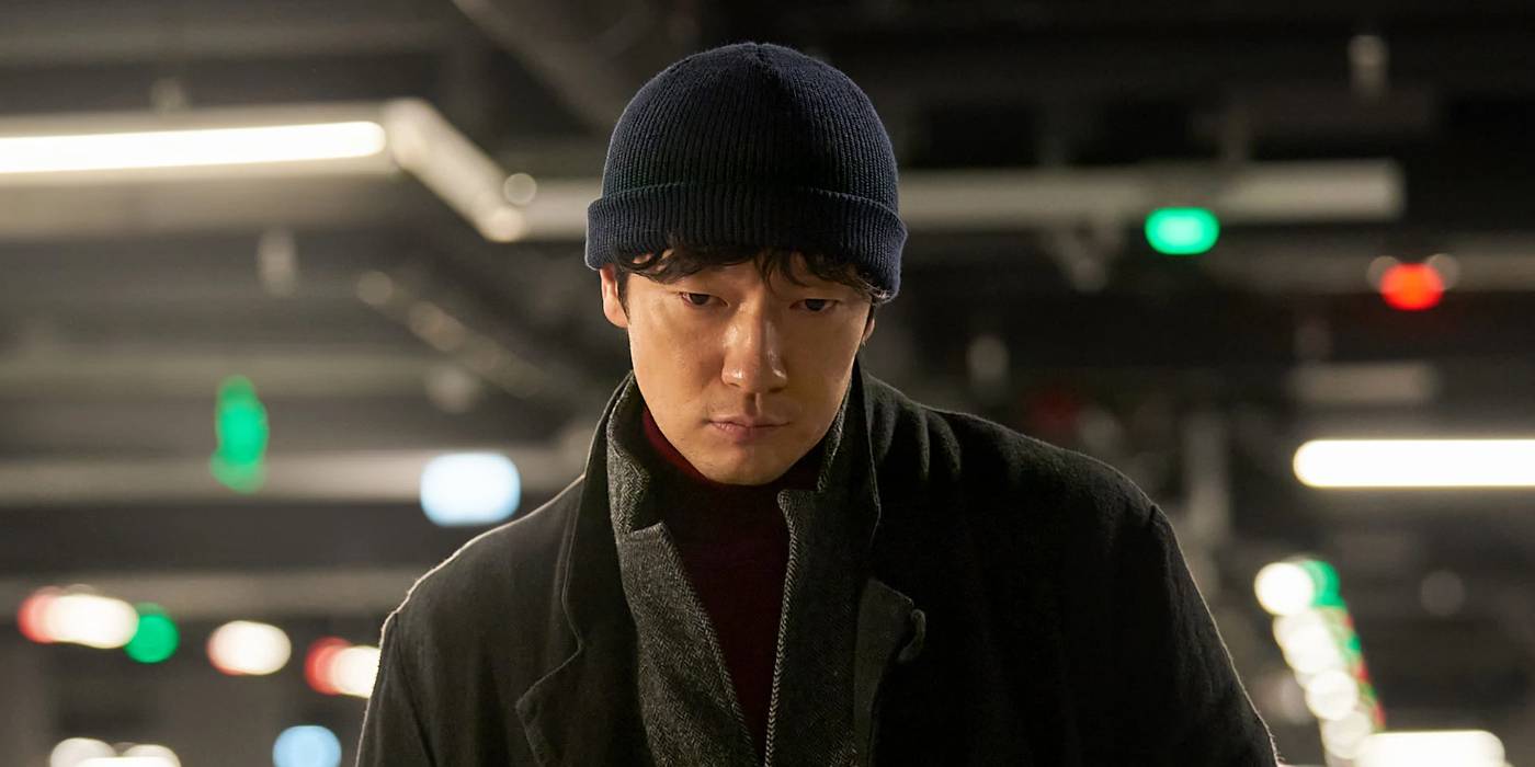 Son Suk-ku standing in an indoor garage watching something off-screen in Nine Puzzles.