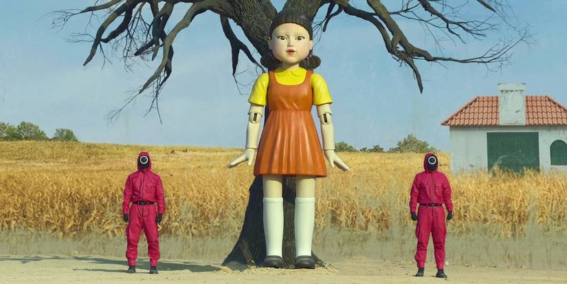 Two soldiers in red flank an oversized doll in Squid Game.