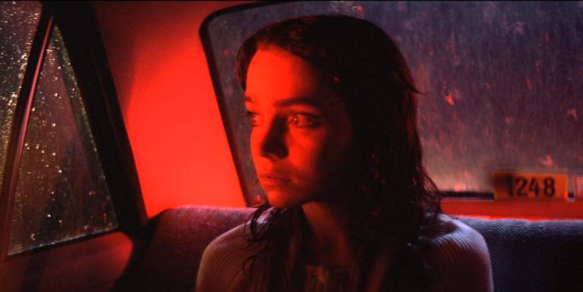 A girl looking scared while on the back of a car bathed in red light in Suspiria