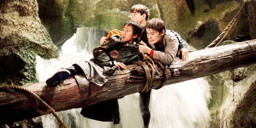 Sean Astin, Ke Huy Quan, and Corey Feldman cling to a log over a waterfall in The Goonies.