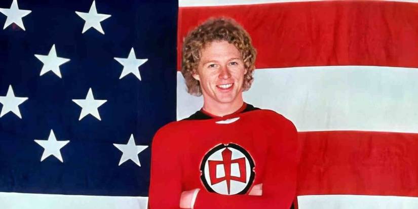 William Katt in a red superhero suit stands in front of an American flag in The Greatest American Hero.