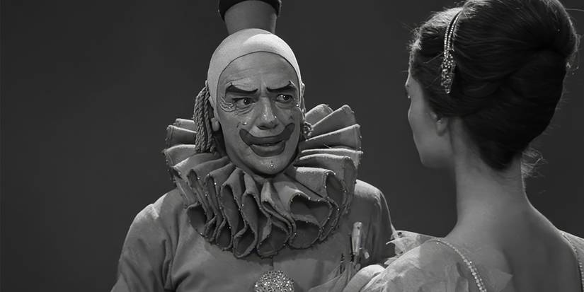 Um homem vestindo uma roupa de palhaço conversando com uma mulher na zona do crepúsculo.
