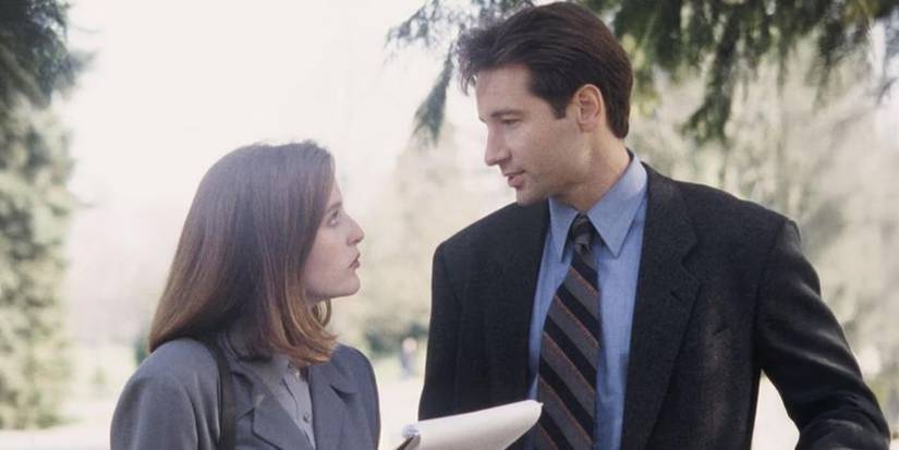 Gillian Anderson and David Duchovny talking outdoors near a tree in the pilot episode of The X-Files.