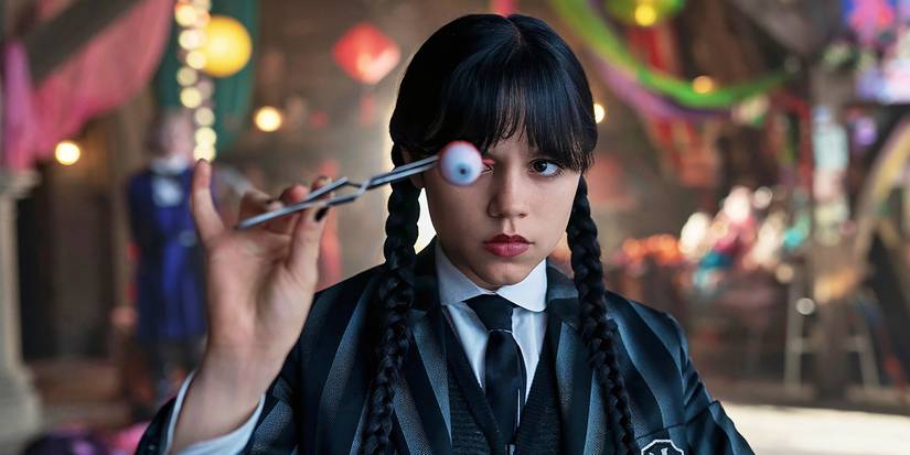 Jenna Ortega as Wednesday wears a Nevermore Academy jacket and holds an eyeball in front of her face