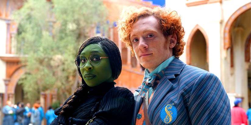 Actors Cynthia Erivo and Ethan Slater as Elphaba and Boq, standing together in the courtyard of Shiz university and posing for the camera in Wicked.
