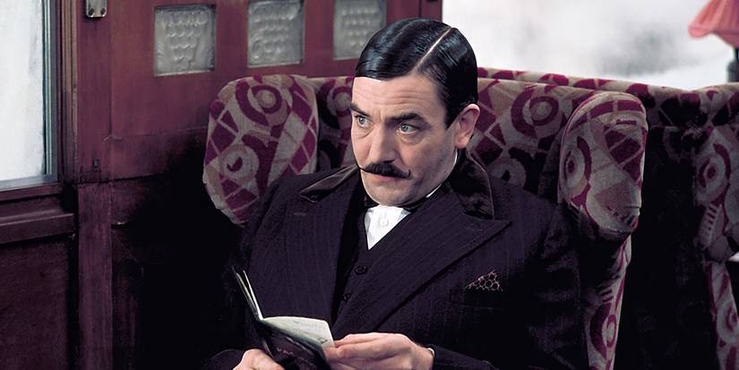 Albert Finney sits on a train, looking up from a small ledger, 1974 Murder on the Orient Express