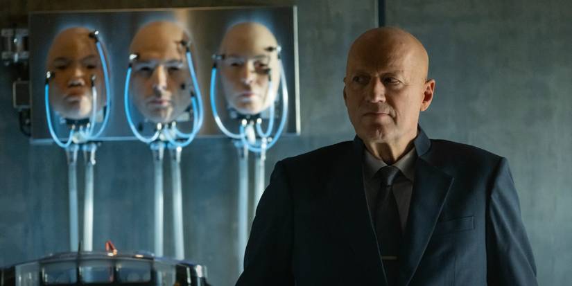 Atom Eins (Adrian Edmondson) stands in front of synthetic faces in Alien: Earth.