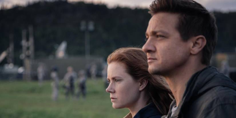 Amy Adams and Jeremy Renner stand side-by-side outdoors and stare ahead in Arrival.